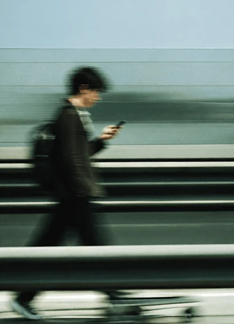 A motion-blurred man walking past a railing while looking at his phone